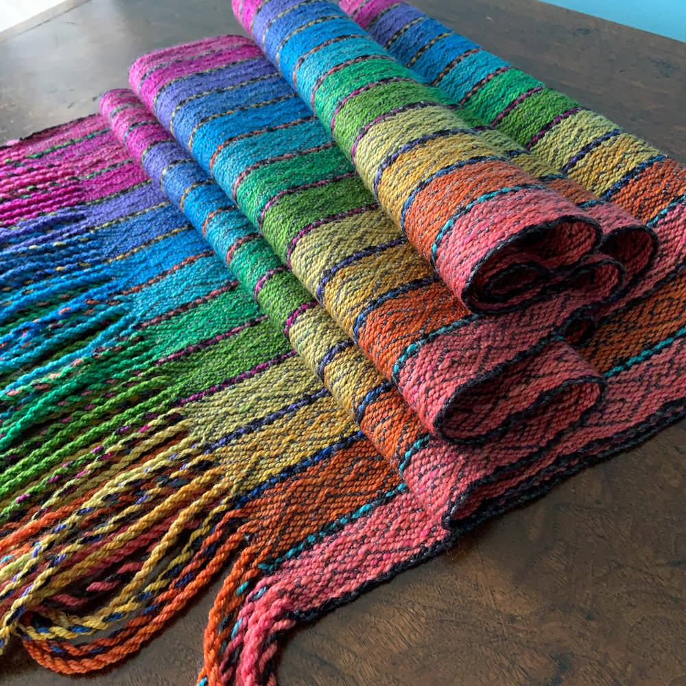 Colorful handwoven rug with rainbow gradient stripes and twisted fringe tassels on wooden floor