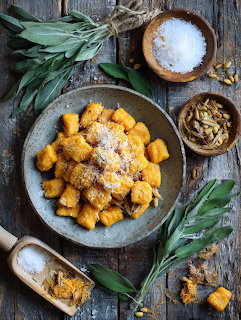 Plate of orange pumpkin gnocchi with parmesan on a rustic wooden surface with sage and condiments