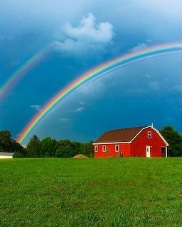 Double rainbow over red barn in green field with stormy sky