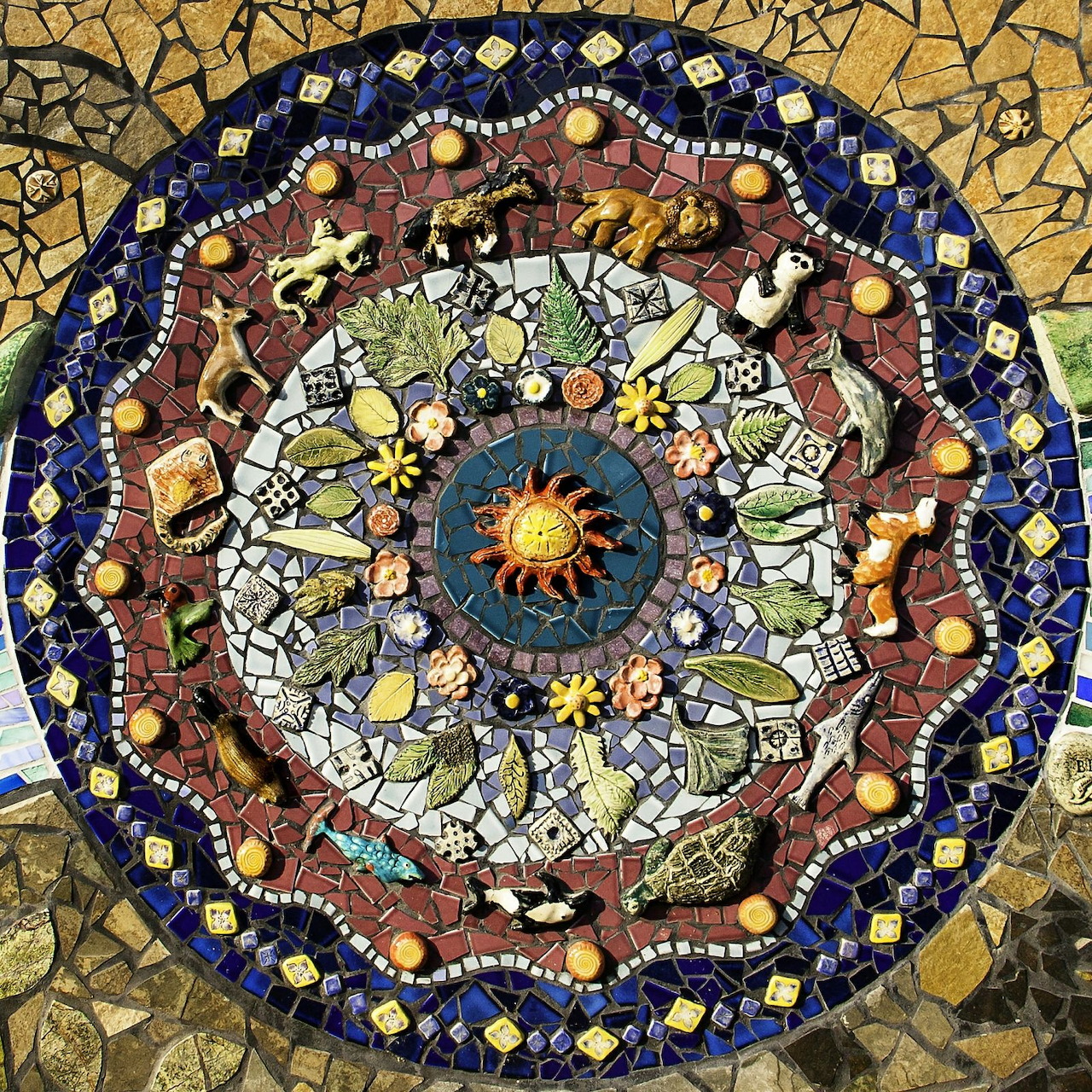 Colorful circular mosaic mandala with central sun design, floral patterns, and peace text on textured golden background