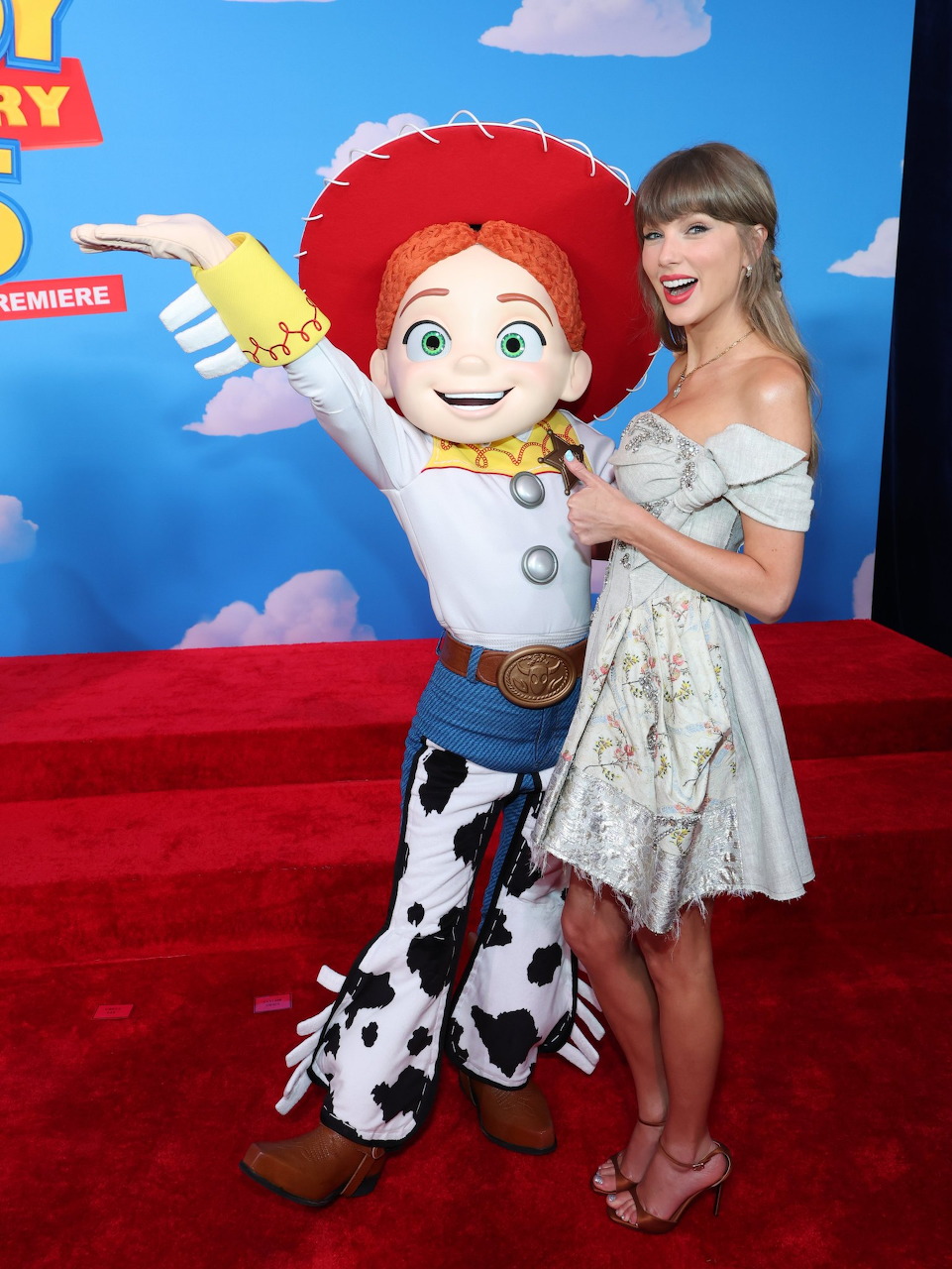 Woman in white dress posing with Jessie character from Toy Story at a movie premiere red carpet