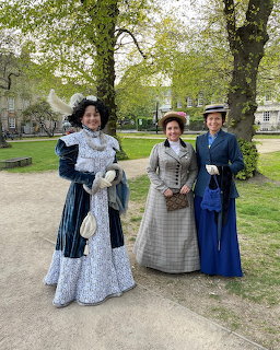 Three women wearing Victorian period costumes posing together in a green park