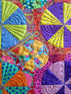 Colorful quilted mandala with geometric fabric sections and decorative spiral stitching in vibrant hues