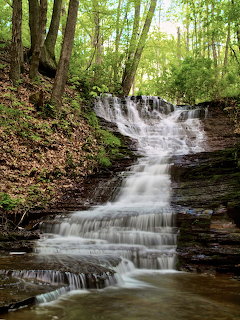 Multi-tiered waterfall cascading over flat rock ledges in a green deciduous forest