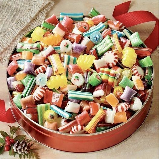 Round box filled with assorted Christmas candies, red ribbon bow, and small pine cone beside it