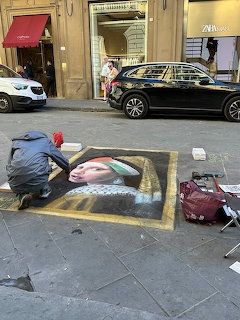 Street artist drawing a chalk painting on a Florence sidewalk with cars and buildings in background