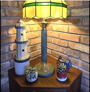 Tiffany-style stained glass lamp on a wooden table with a lighthouse model and two small potted plants