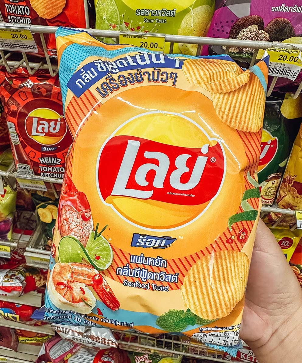 Hand holding orange Lays seafood twist chips bag in Thai convenience store