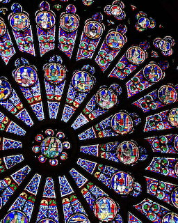 Ornate circular stained glass rose window with radial gothic design in brilliant blues, reds, and purples