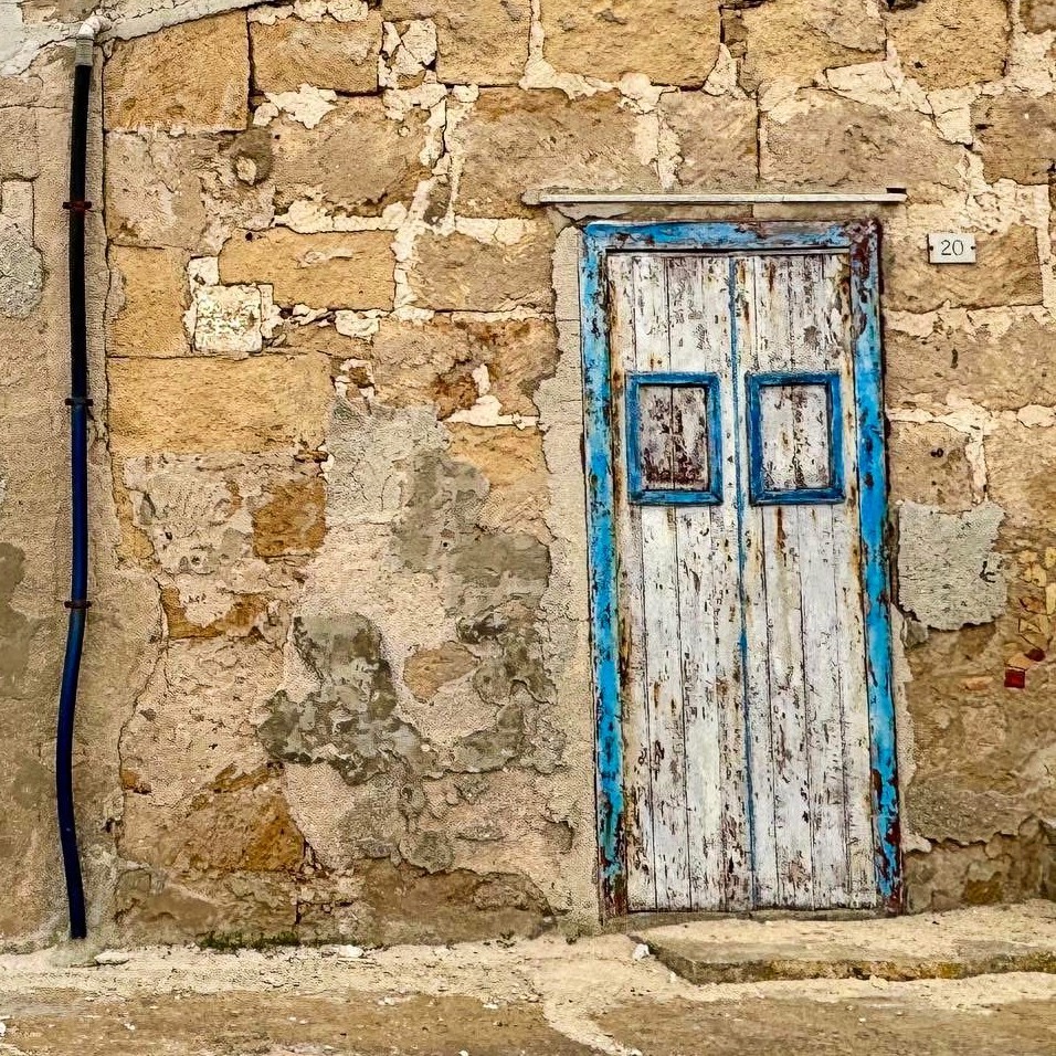 Old blue wooden door with peeling paint in weathered stone wall, Sicily