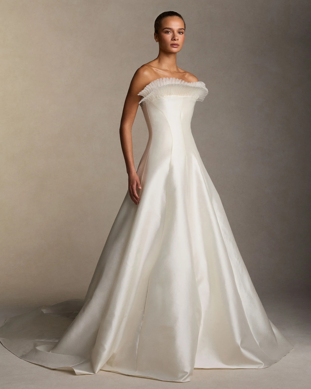 Model wearing an off-shoulder white A-line wedding dress against a beige backdrop