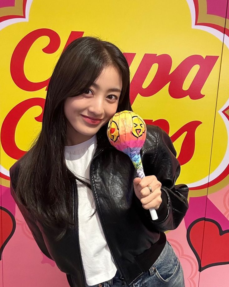 Smiling young woman holding a giant Chupa Chups lollipop in front of a pink and yellow branded background
