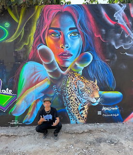 Colorful street art mural of a blue woman with multicolored hair and a jaguar, man posing in front