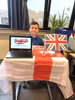 Boy sitting at a classroom table with British flags, a laptop, and a red and white tablecloth.