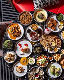 Overhead flatlay of colorful brunch dishes including eggs, pancakes, salads, breads, and desserts on various plates