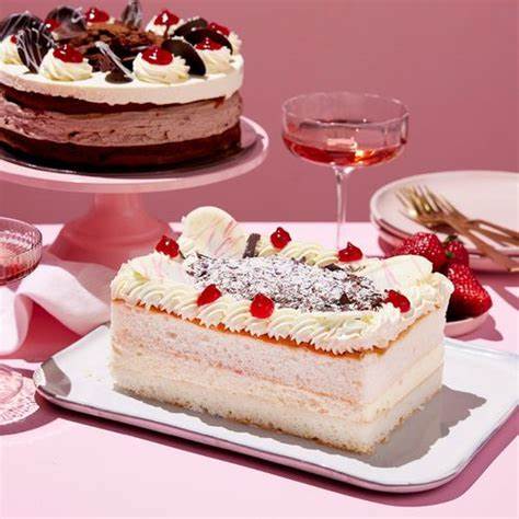 Rectangular strawberry cream cake on a tray with whipped topping, cherries, and a pink table setting