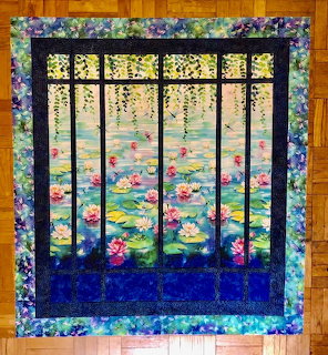 Quilted wall hanging with black window frame looking out at water lilies on pond with decorative floral border