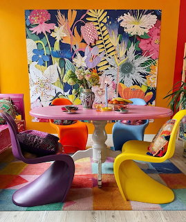 Bright dining room with floral artwork, round table, and colorful modern chairs