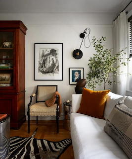Cozy living room with white sofa, orange pilow, vintage chair, wall art, and indoor plant near a window
