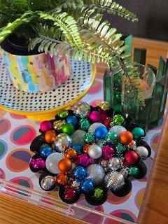 Colorful shiny Christmas ball ornaments piled in a clear box next to a poted fern plant