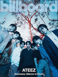 Eight members of ATEEZ posing together outdoors with red tree branches and dark blue sky behind them