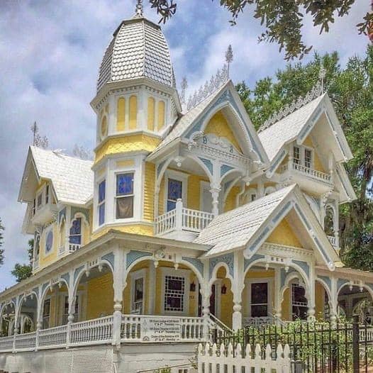 Pale yellow Victorian house with a turret, decorative trim, and wraparound porch