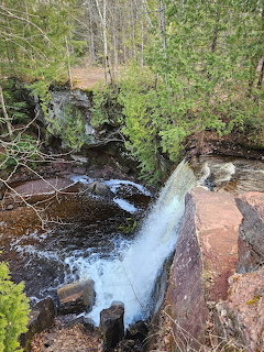 Waterfall flowing over dark rocks in a forested area with moss and birch trees