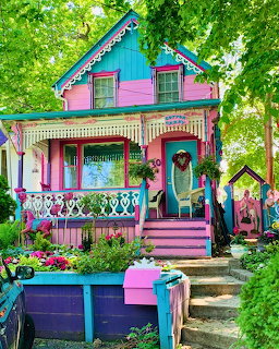 Brightly painted pink and teal Victorian cottage with decorative trim and colorful garden