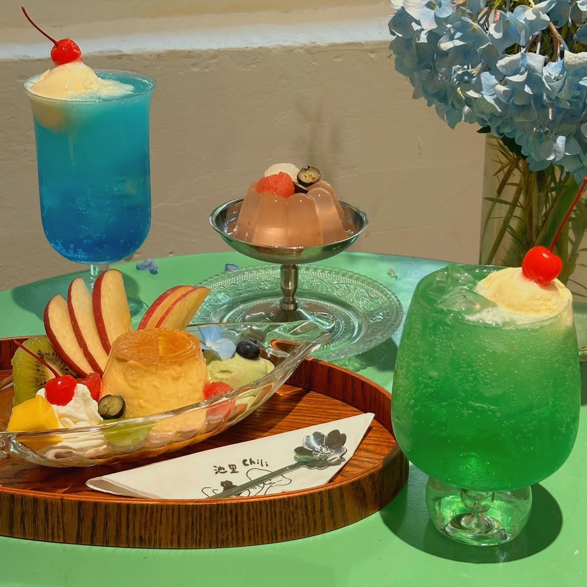 Blue and green cocktails with red cherries and tropical desserts on wooden tray