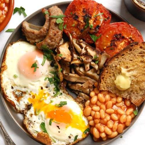 Overhead view of a traditional English breakfast with eggs, sausages, mushrooms, tomatoes, beans, and toast on a plate