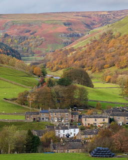 Stone village in a green valley with autumn-colored hills behind