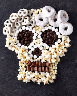 Skull-shaped Halloween charcuterie board made from white donuts, marshmallows, chocolates arranged on dark background