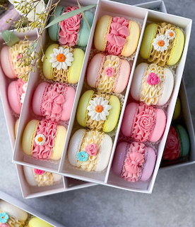 Rows of pastel decorated macarons with piped flowers and daisies arranged in white gift boxes