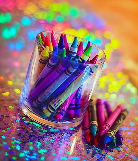 Bright crayons in a glass on a glittery surface with colorful blurred lights