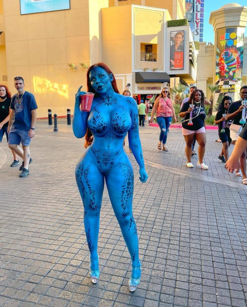 Woman covered in blue body paint with dark patterns posing outdoors at an entertainment venue