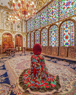 Woman in floral dress viewing elaborate stained glass windows in Persian palace interior with ornate tilework and chandelier