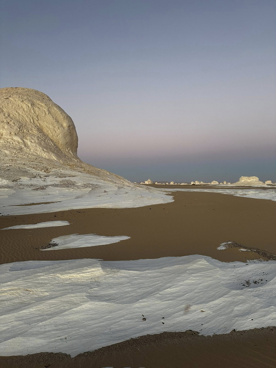 White chalk rock formations rise above sandy desert floor in Egypt's White Desert at dusk