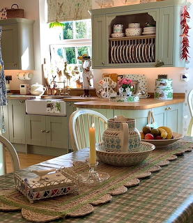 Country kitchen with green cabinets, plate rack, wooden countertops, and a set dining table with candle and fruit bowl
