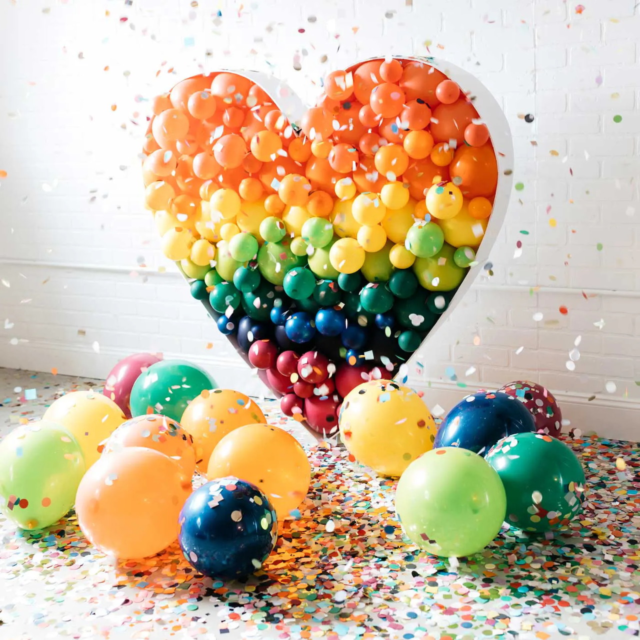 Heart-shaped rainbow balloon display with colorful balloons and confetti on the floor