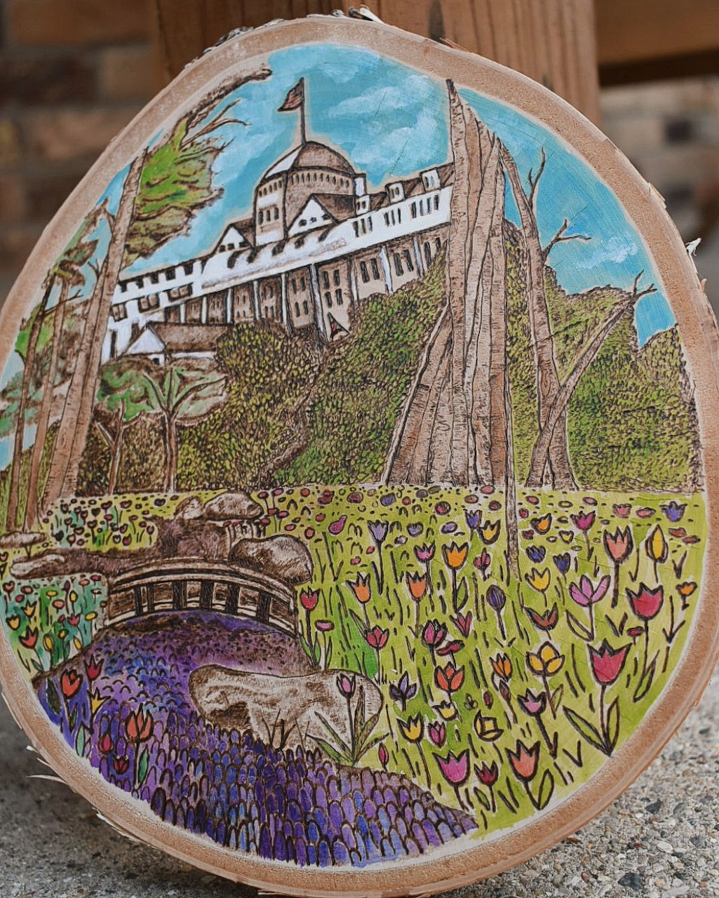 Embroidery hoop art of garden path leading to white Victorian building with flowers and trees