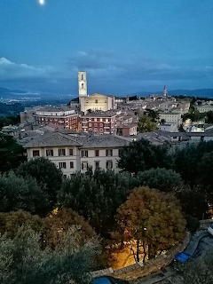 View of Perugia at dusk with historic buildings, a church tower, and trees in the foreground