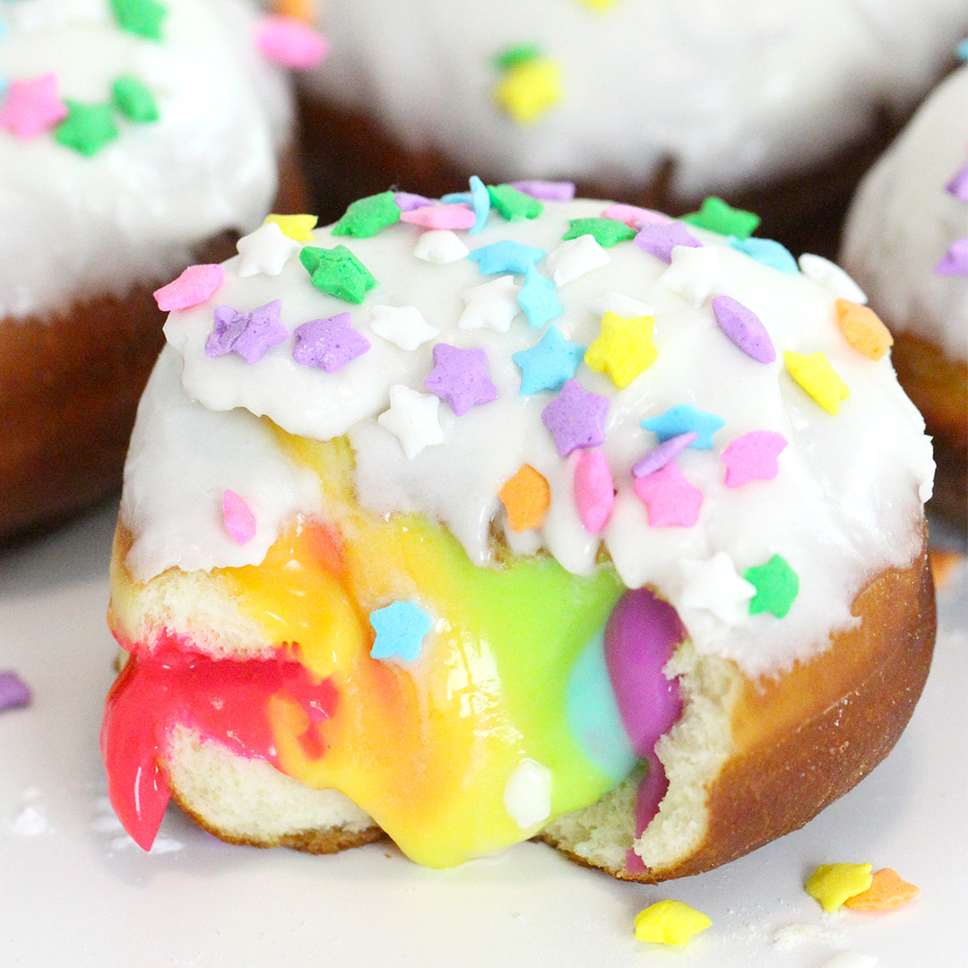 Frosted donut with rainbow filling and colorful sprinkles on white background