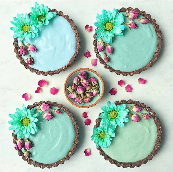 Four turquoise frosted cakes with blue flowers and pink rosebuds around a bowl of dried rosebuds