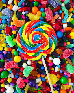 Rainbow spiral lollipop centered among colorful assorted candies and gummy sweets