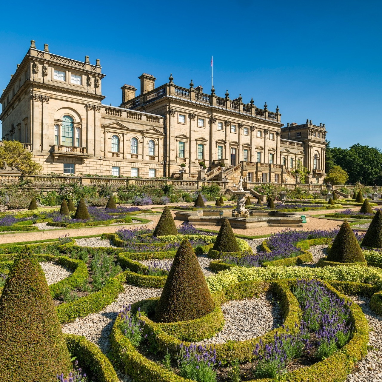 Stately baroque mansion with formal geometric gardens featuring sculpted hedges and topiary in foreground