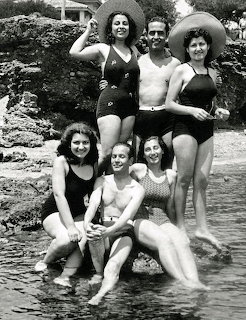 Black and white vintage photo of six people posing at a rocky seaside shore in swimwear