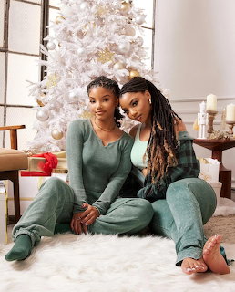 Two women in green loungewear posing together by a white Christmas tree