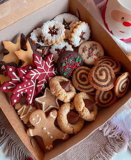 Cardboard box filled with assorted Christmas cookies including gingerbread, iced snowflakes, and pinwheel cookies