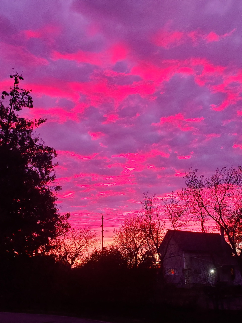 Vibrant pink and purple sunset sky over silhouetted trees and a rural house