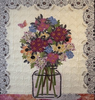 Fabric quilt showing mixed flowers in jar vase with lace border